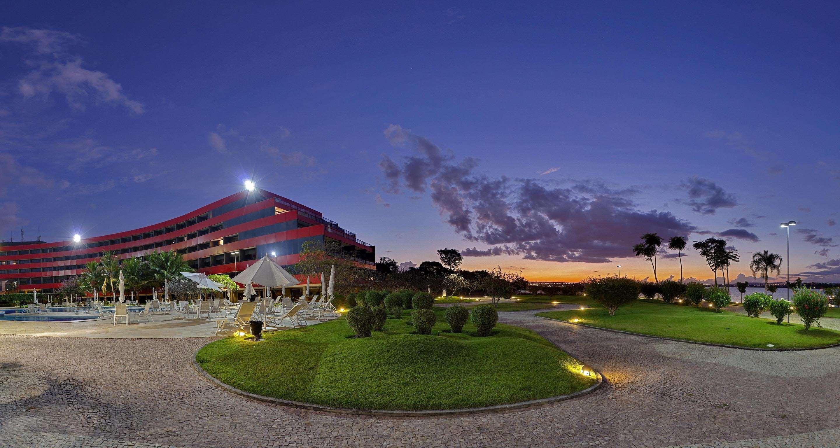 Royal Tulip Brasilia Alvorada Hotel Luaran gambar The photo depicts a modern building, possibly a hotel or resort, with a striking red exterior. It is set in a landscaped area that features well-maintained greenery and ornamental plants. In the foreground, there are lounge areas with umbrellas, sugg